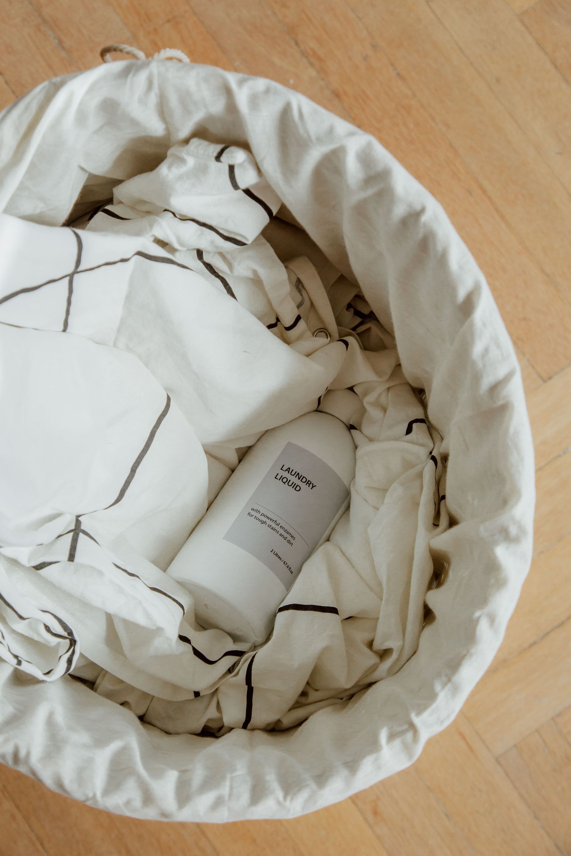 White laundry basket filled with crumpled white paper and a small bottle on a wooden floor