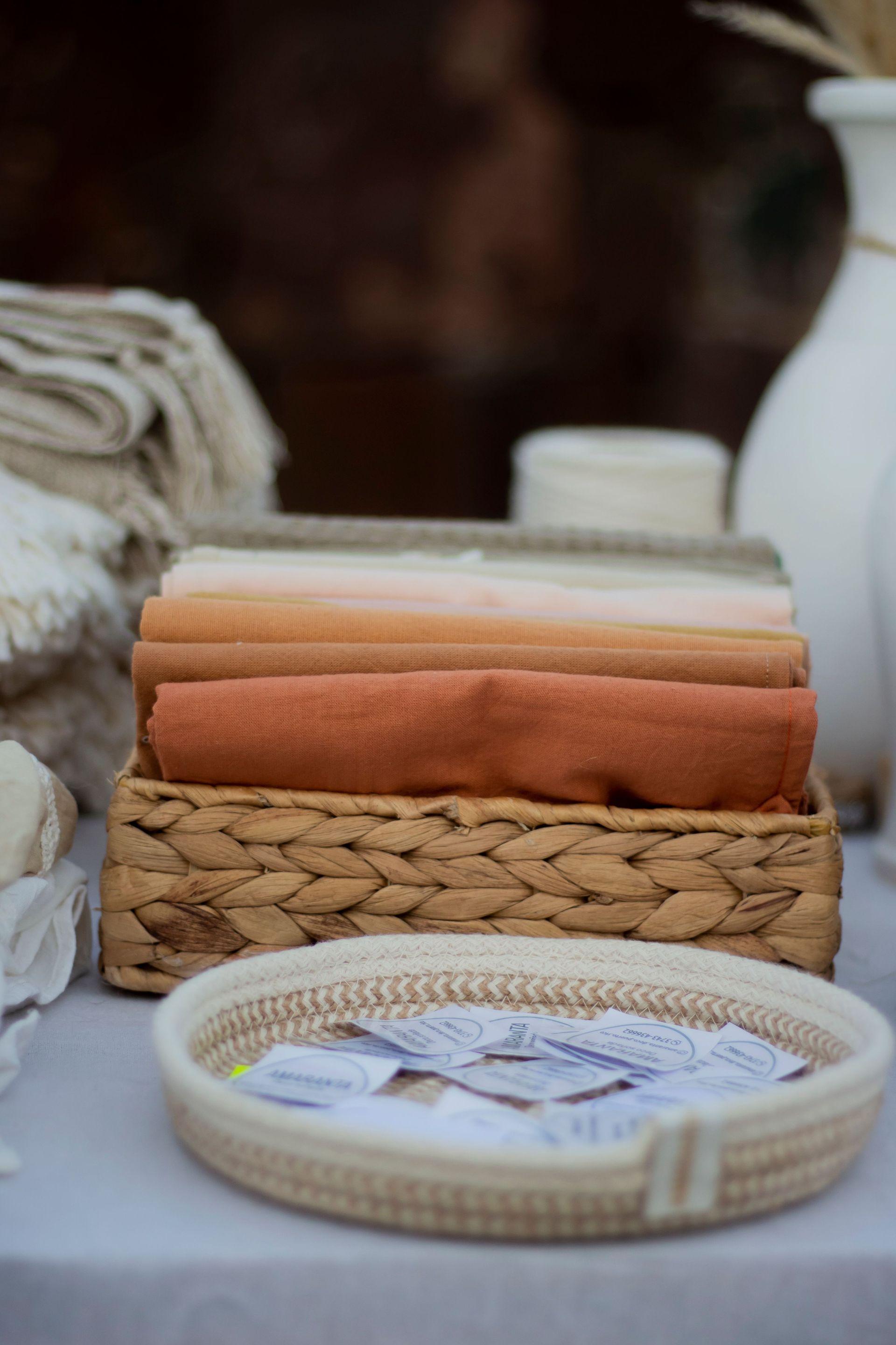 Woven trays with folded beige and orange towels and a small dish of wrapped soaps on a table