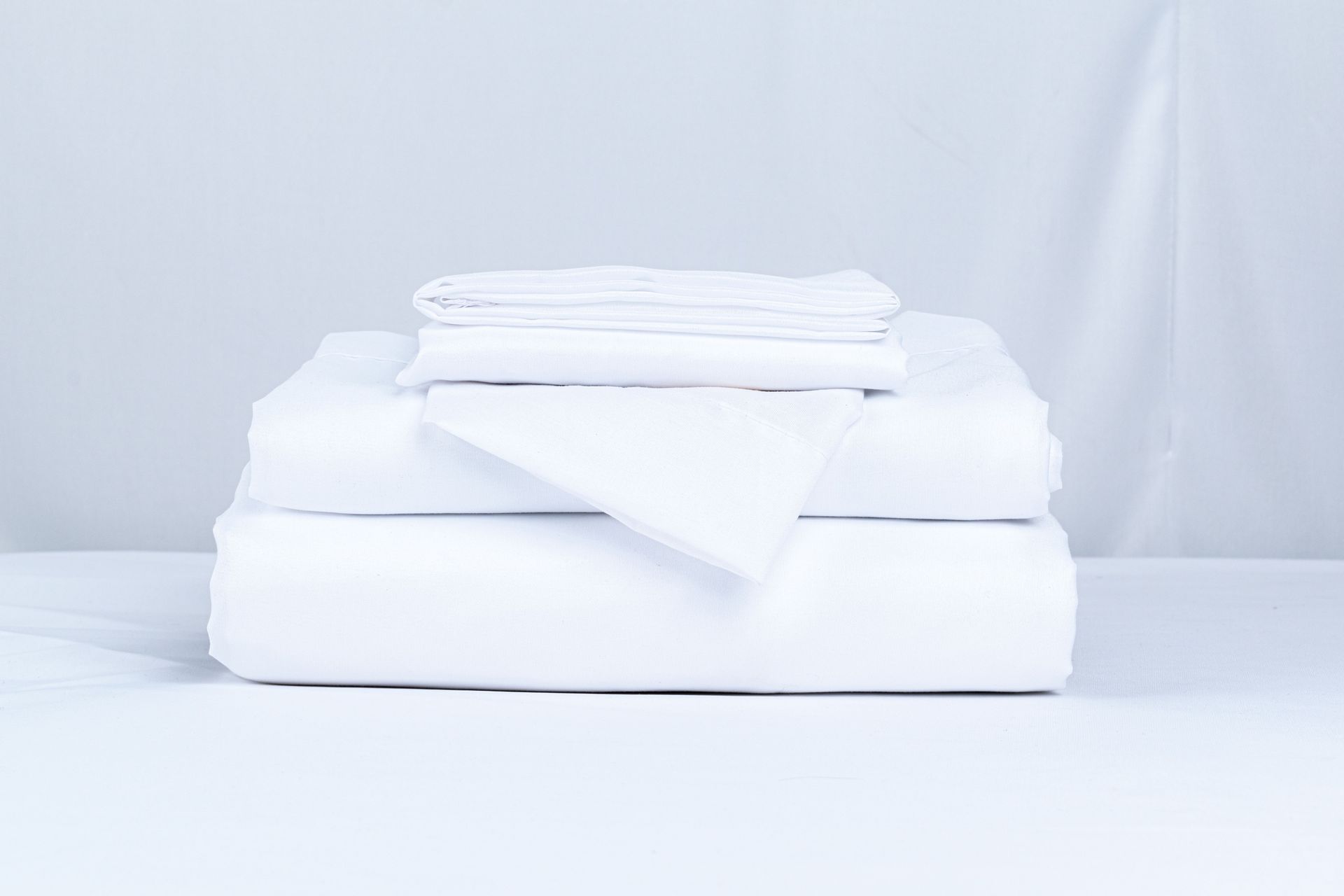 Neatly folded white towels stacked on a white bed against a light gray background