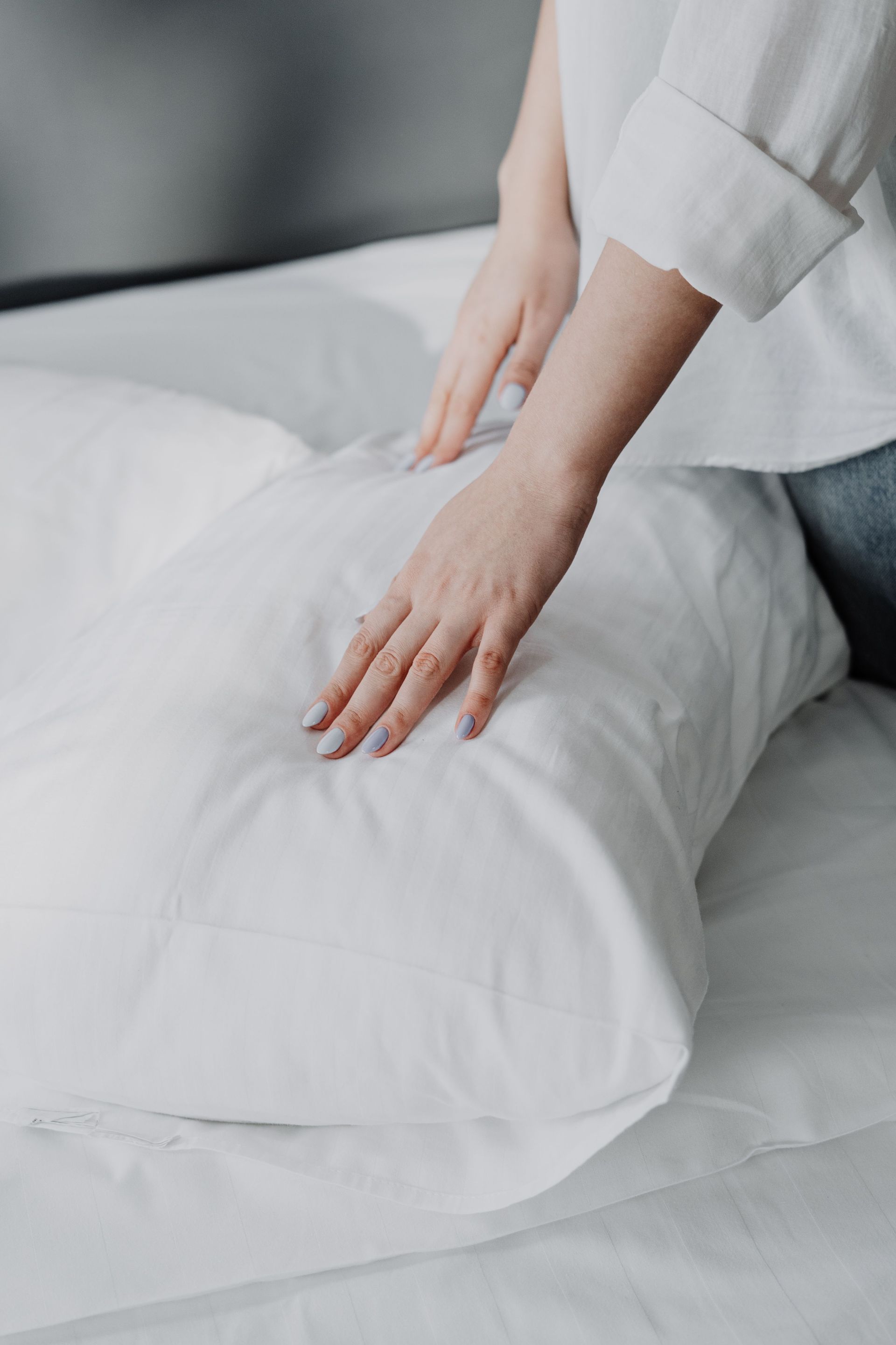 Hands smoothing a white pillow on a bed with white bedding