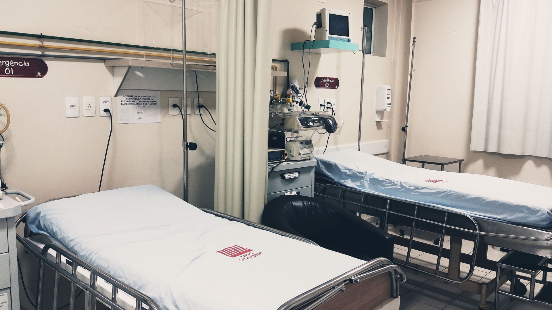Empty hospital room with two beds, privacy curtain, wall monitors, and medical equipment