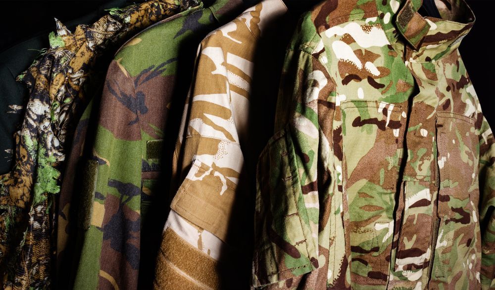 Camouflage jackets hanging on a clothing rack, showing green, tan, and brown military-style patterns