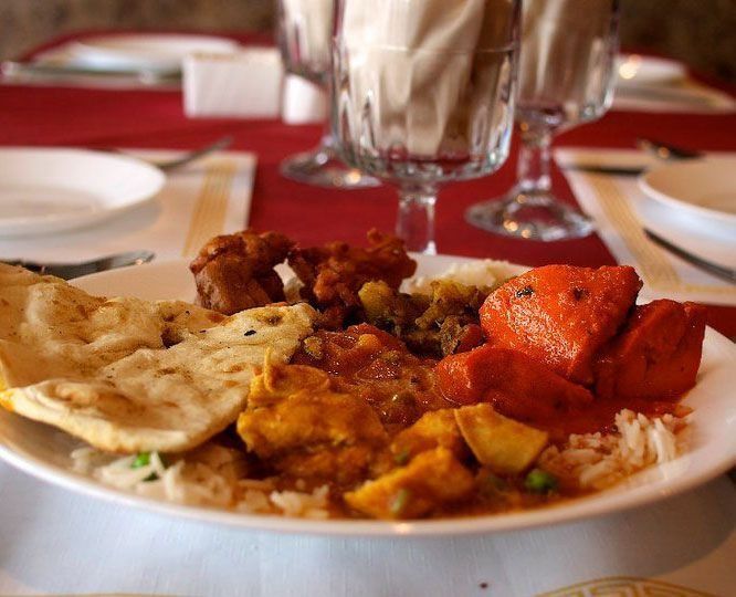 Plate of Indian food: naan, rice, curry, and tandoori chicken on a white plate in a restaurant setting.