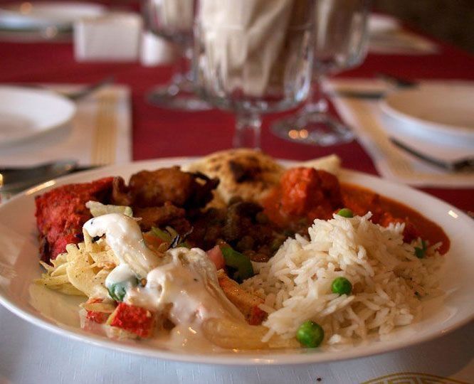Plate of Indian food: rice, chicken, naan, and vegetables on a table with a red tablecloth.