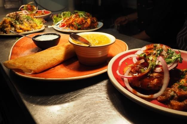 Plates of Indian food: dosa, curry, yogurt, and other dishes on a stainless steel surface.