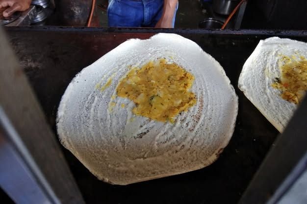 Dosa with potato filling on a hot griddle, close-up.