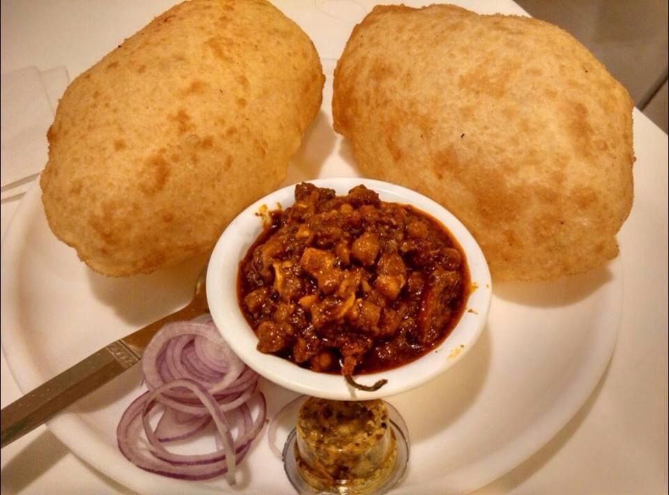Two puffed Indian breads, chole (chickpea curry), onion slices, and condiments on a plate.