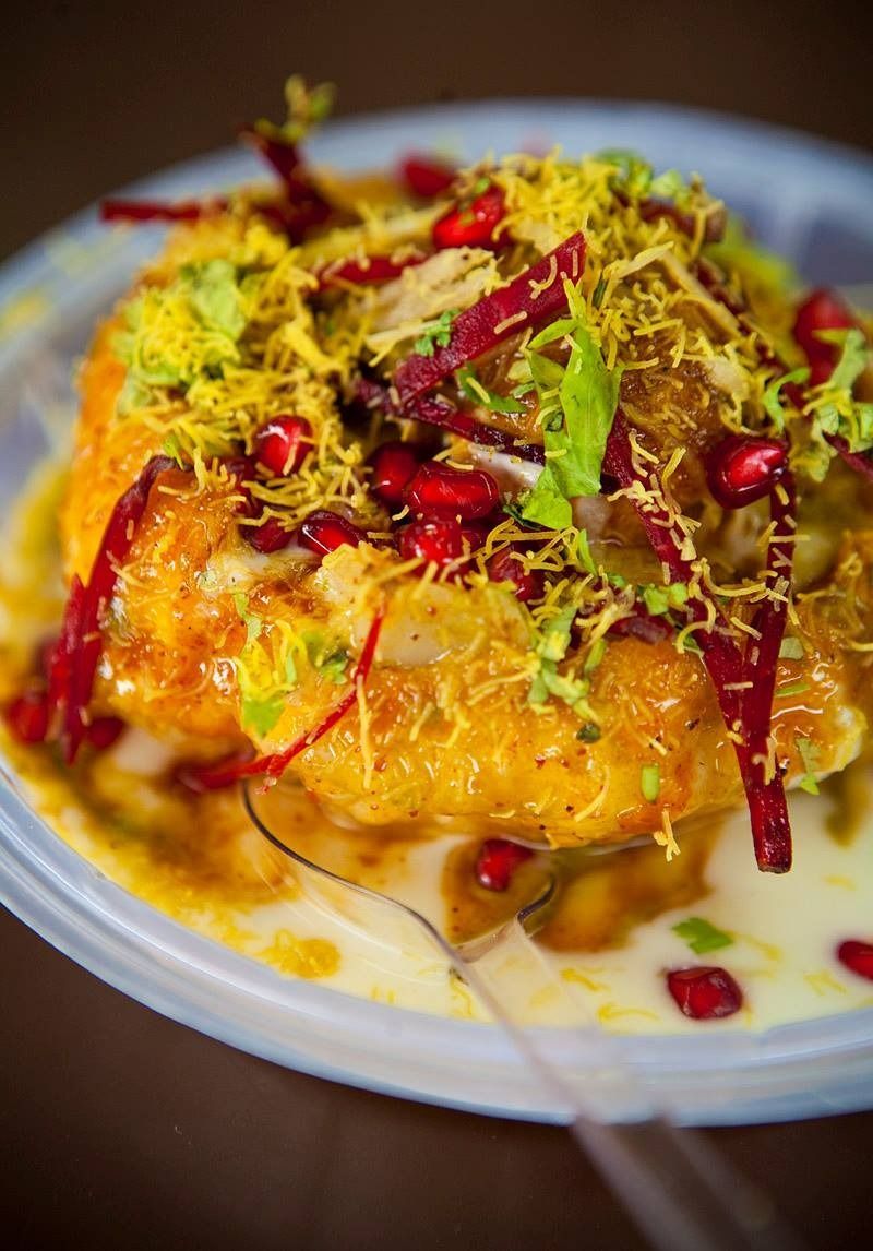 Close-up of a golden-brown, round fried food topped with various garnishes, served in a clear plastic container.