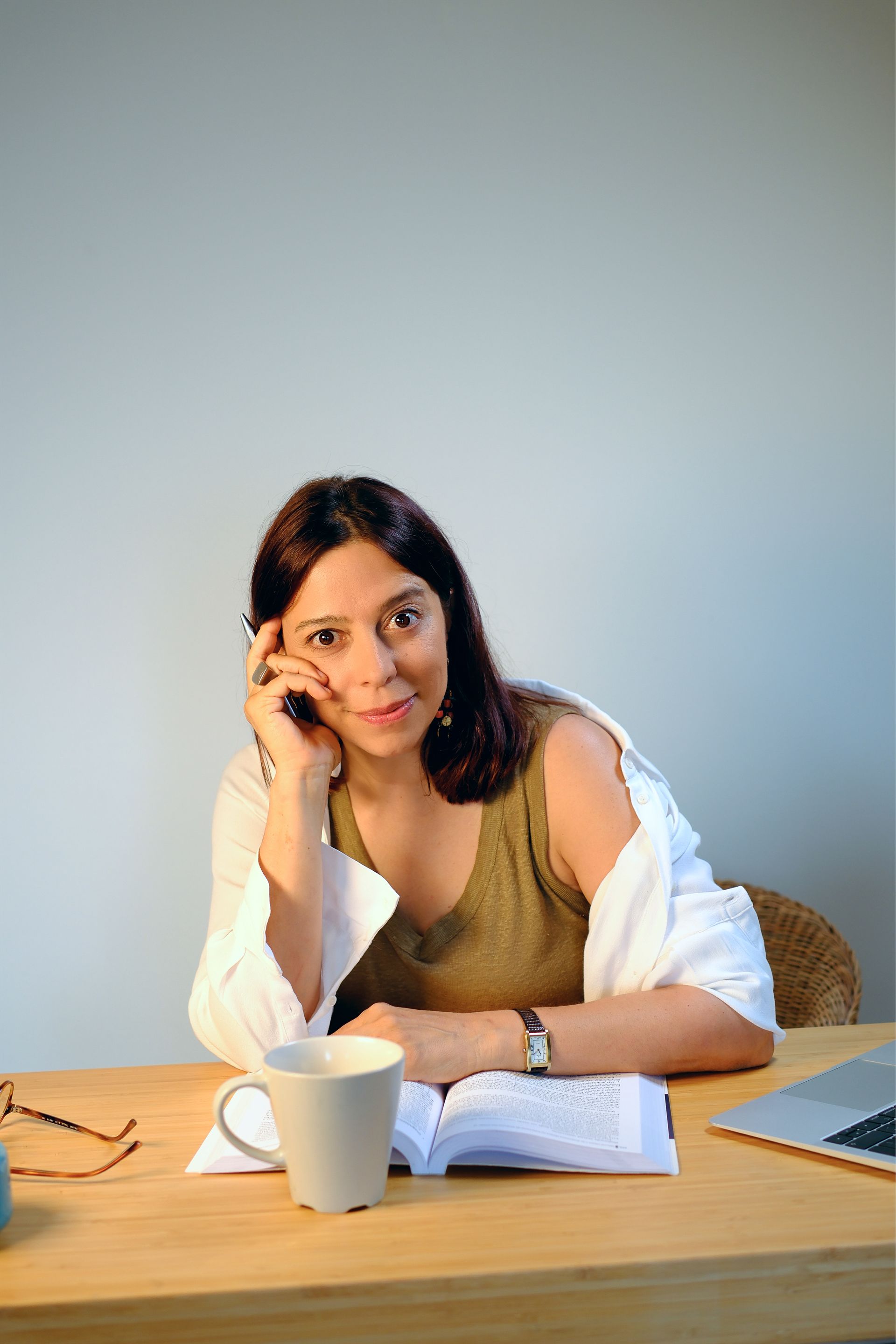 Woman sitting at a table, resting on her hand and looking at the camera.
