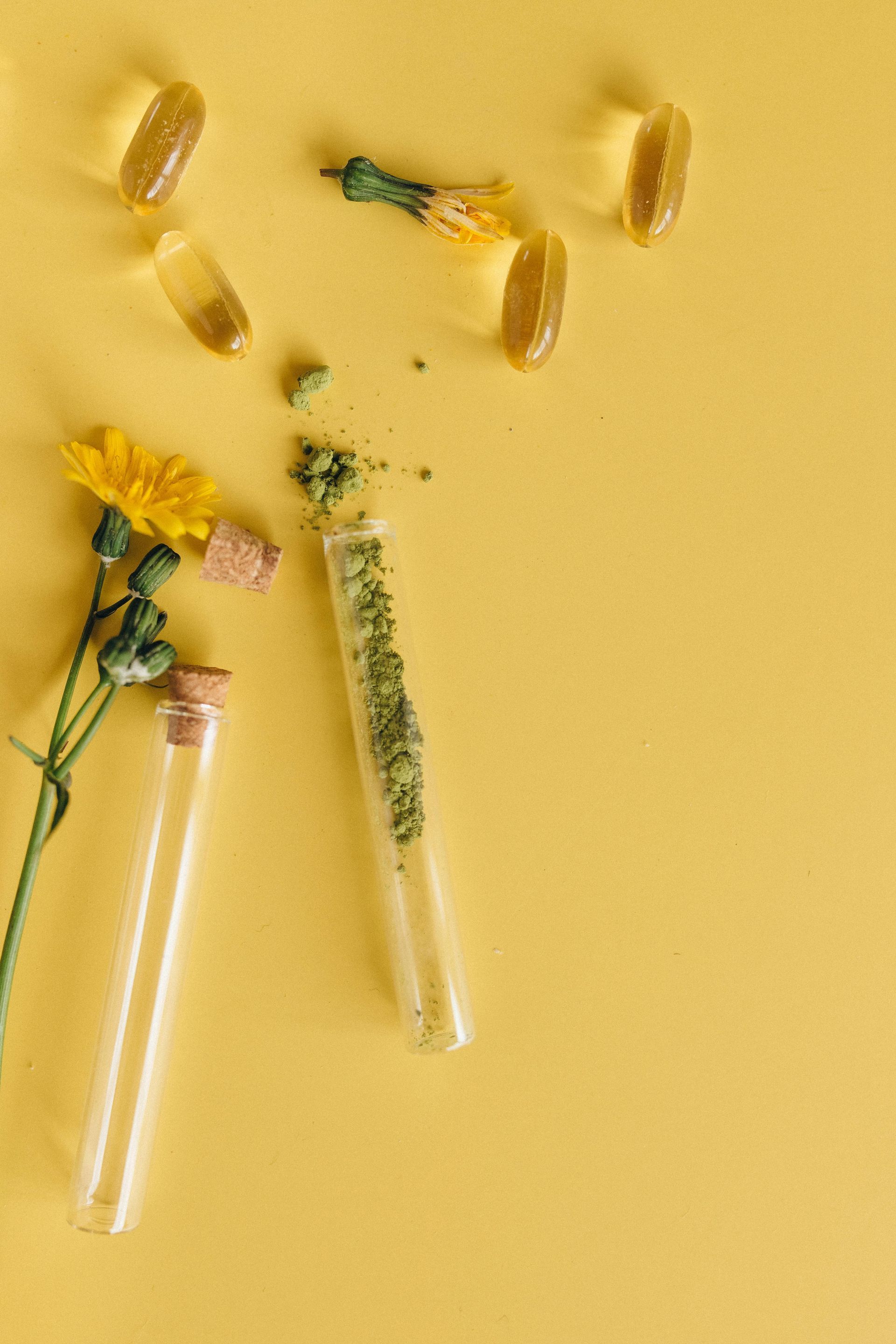 Yellow background with capsules, test tubes with ground green substance, and yellow flowers.
