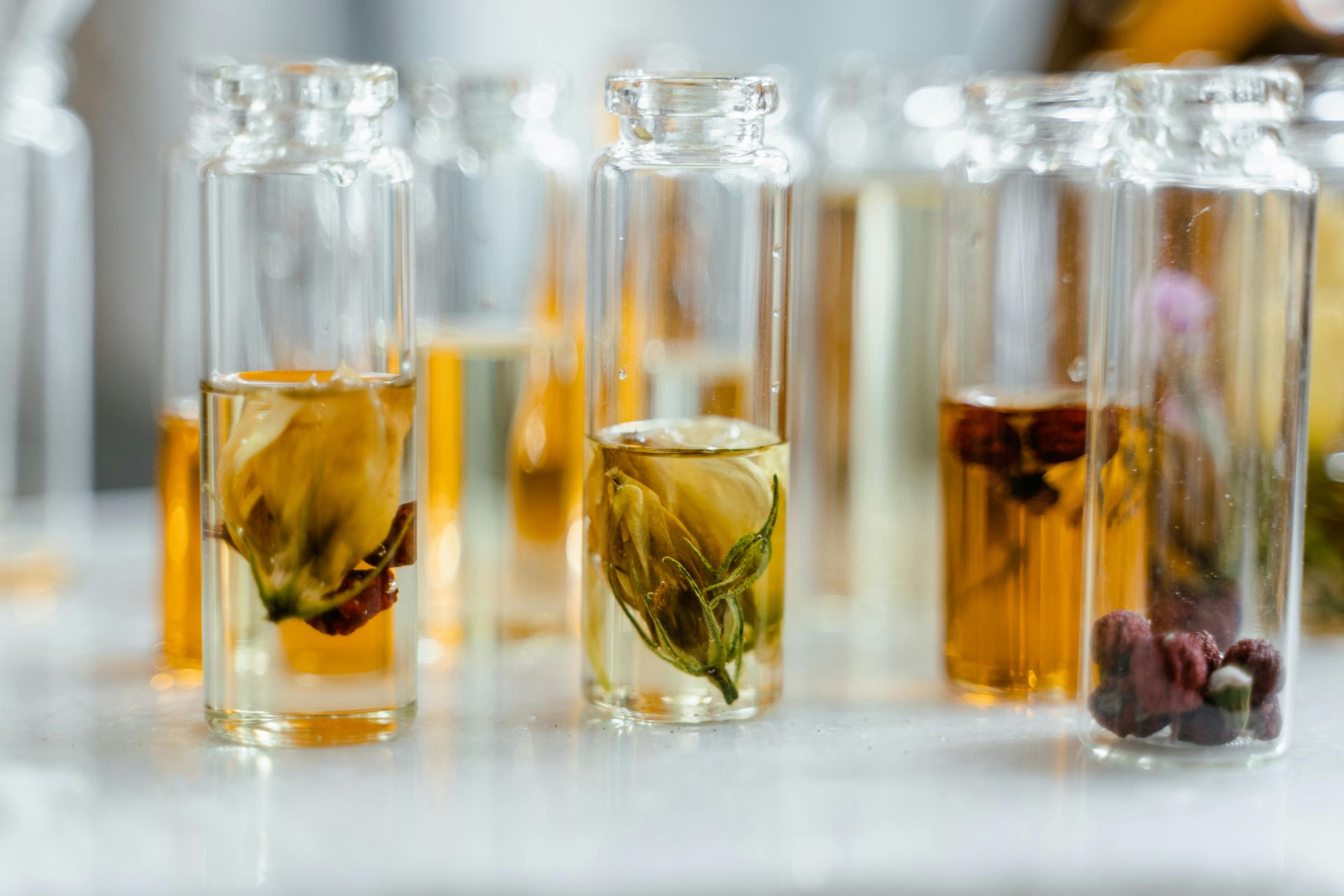 Glass bottles filled with a yellowish liquid containing dried flowers are on a white surface.