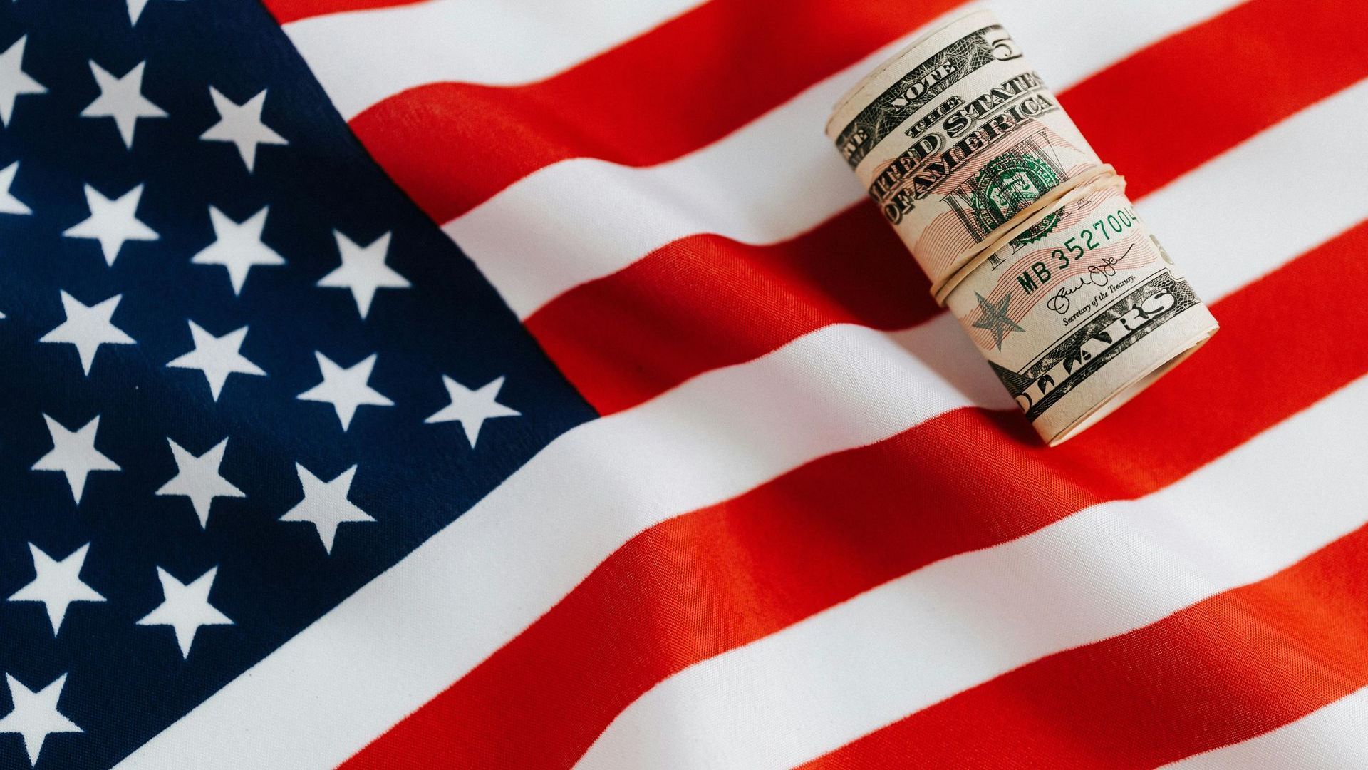 A roll of money is sitting on top of an american flag.
