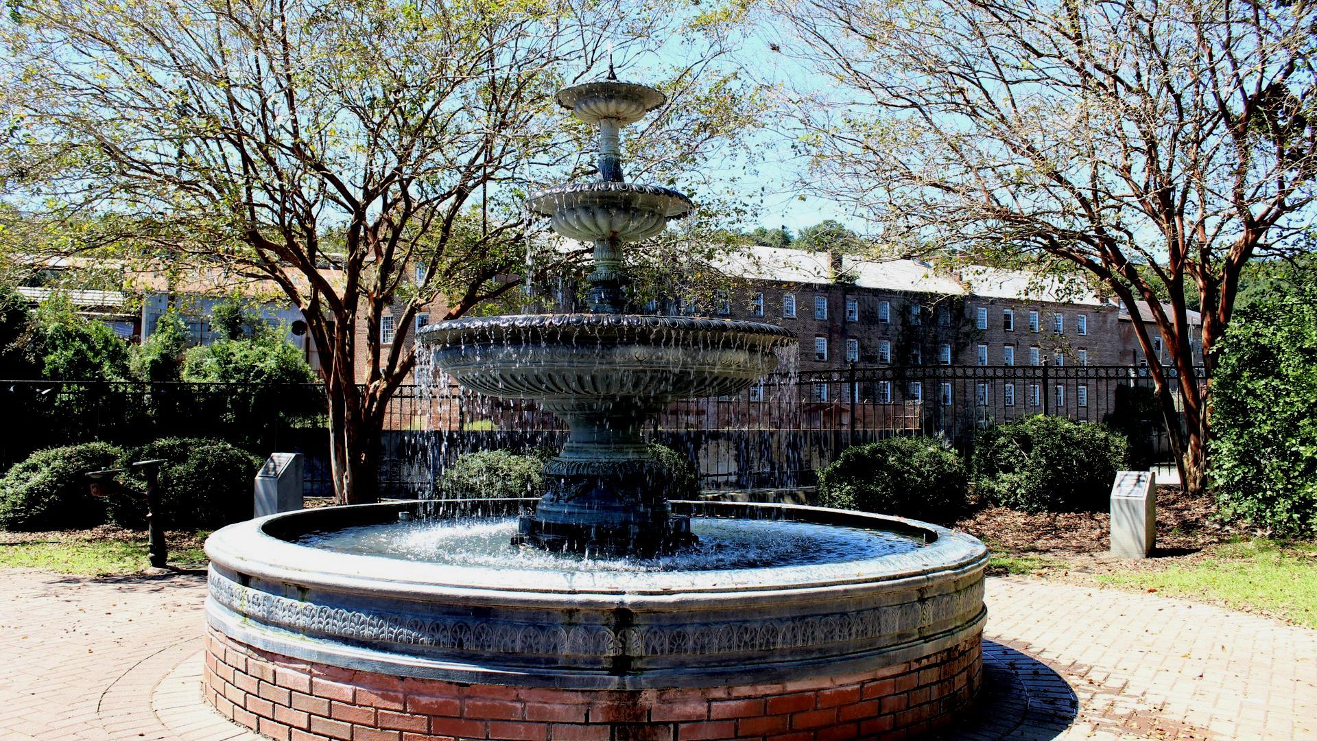 A large fountain is surrounded by trees in downtown park.