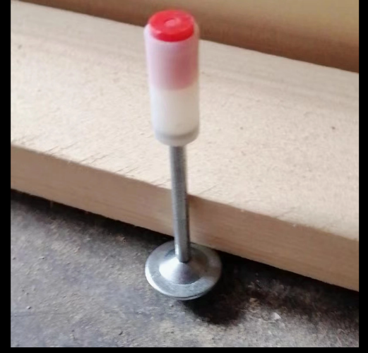 Una pequeña clavija metálica con una tapa blanca de color rojo se encuentra junto a una tabla de madera