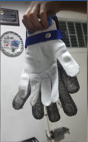 Guante de trabajo de punto gris sujetando una superficie metálica, con el puño azul visible.