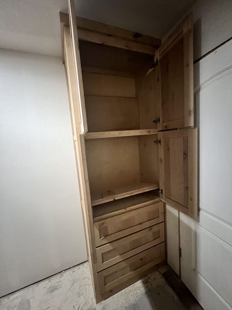 Open wooden cabinet in a bare room, with shelves above and drawers below.