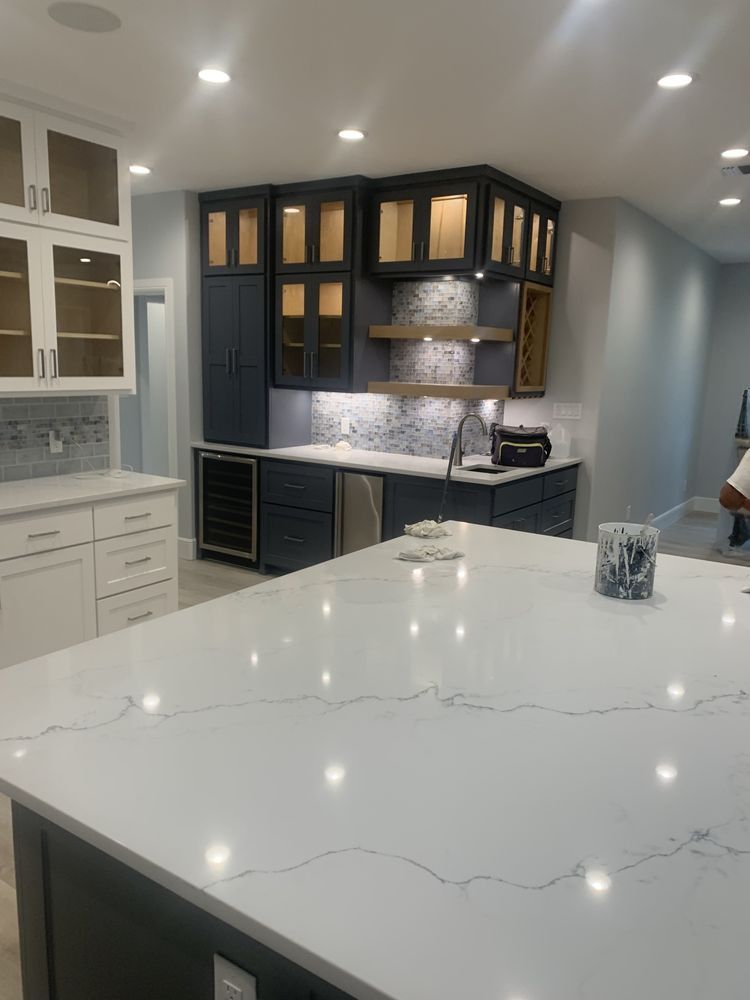 Modern kitchen with white marble island, dark cabinets, and warm-lit open shelving