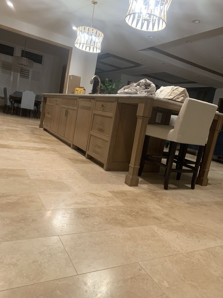 Modern kitchen with tiled floor, island counter, pendant lights, and a white bar stool at right.