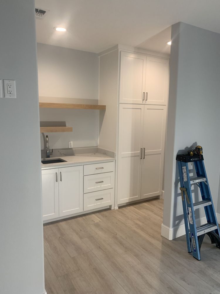 Small kitchen alcove with white cabinets, wood floor, and a blue ladder on the right