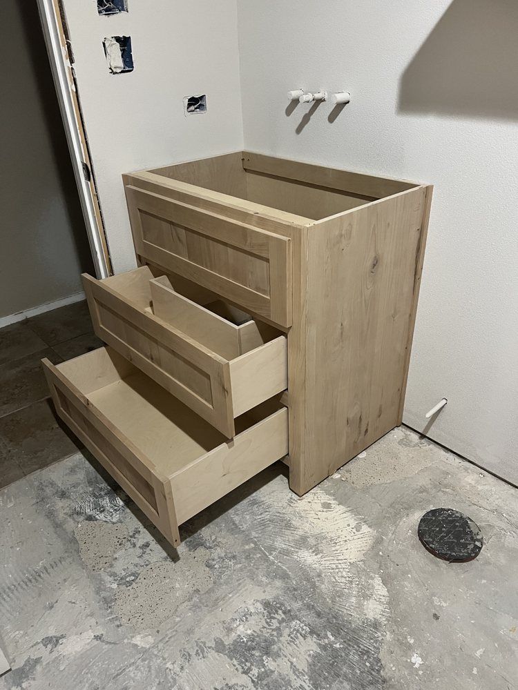 Partially assembled light wood dresser with open drawers in a bare room under construction