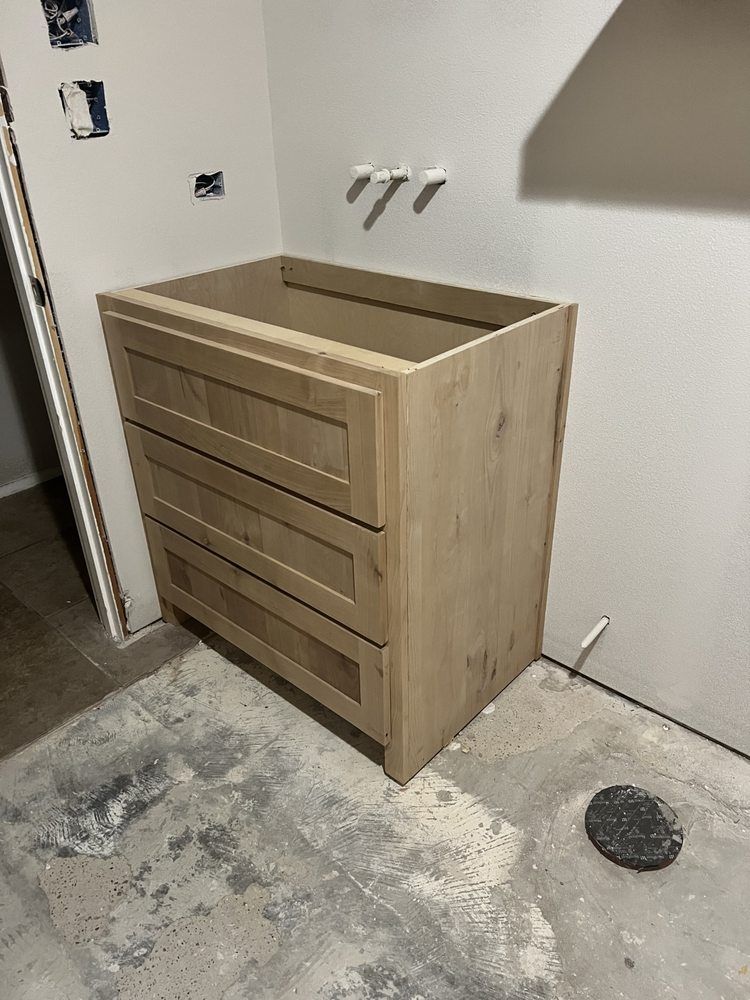 Wooden storage cabinet with drawers against a white wall in a concrete-floored room