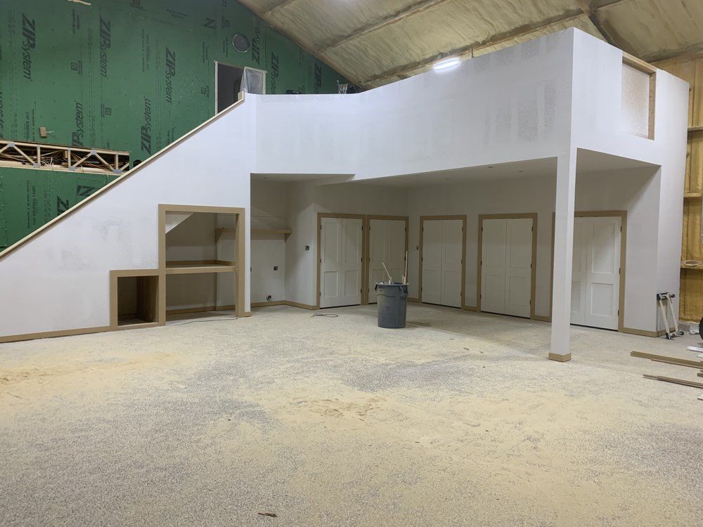 Indoor warehouse-like room with a white loft structure, stairs, doors, and a covered area below.