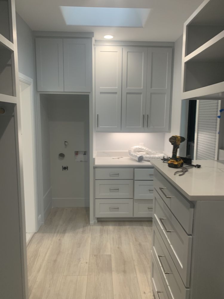 Narrow walk-in closet with white cabinets, drawers, and built-in shelving on both sides.