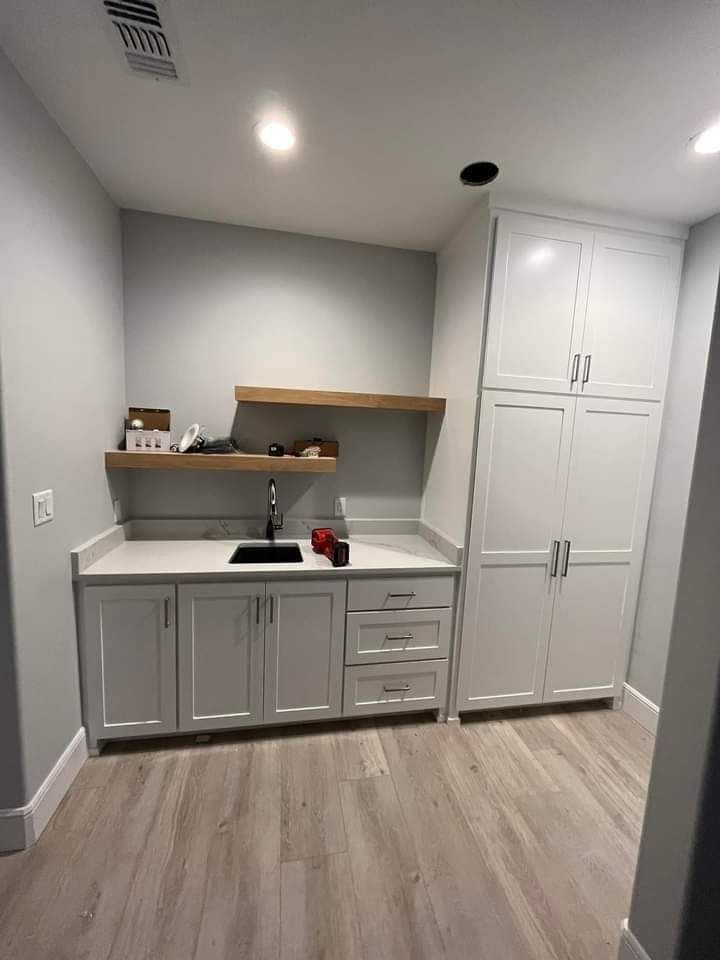 Small gray home office with cabinets, desk, floating shelf, and wood flooring.