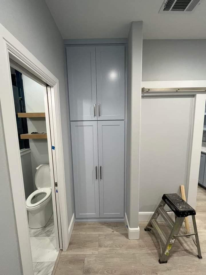 Bathroom under renovation with gray built-in cabinet, open doorway, and a step stool on wood-look flooring.