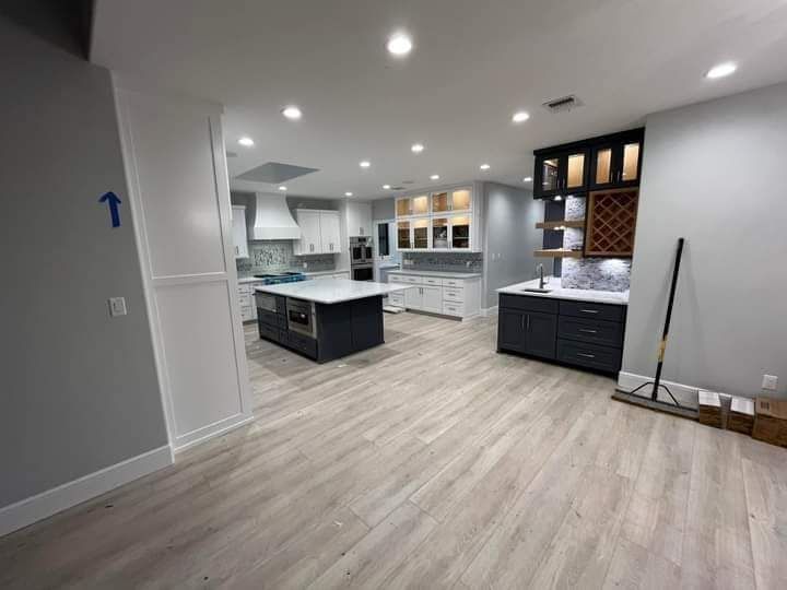 Spacious modern kitchen with white cabinets, black island, and light wood flooring.