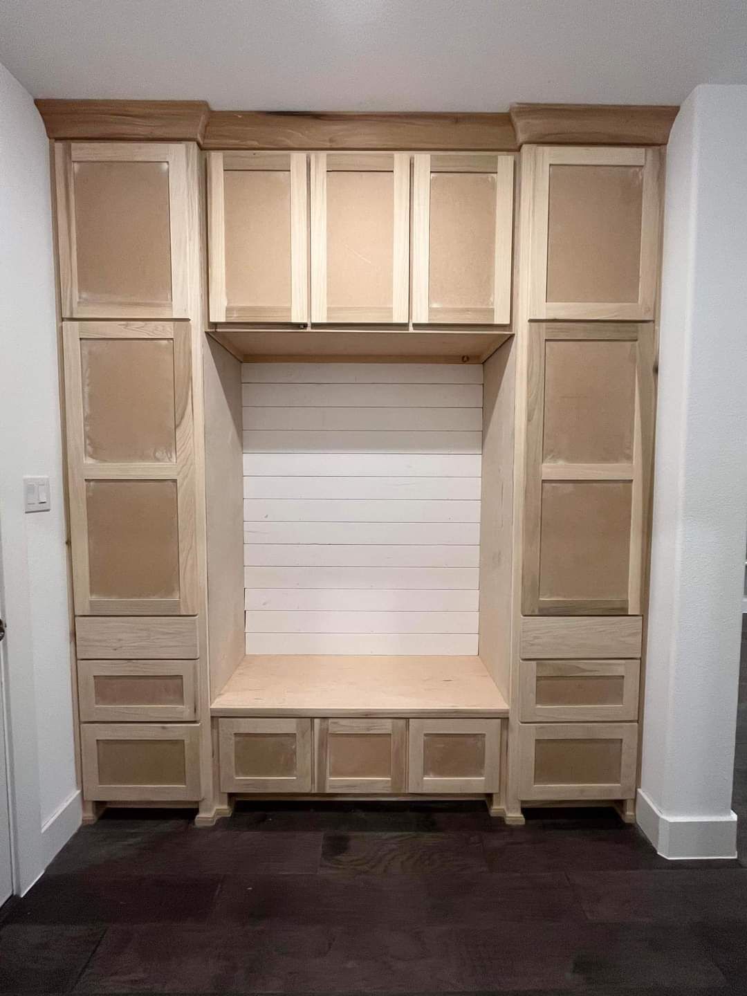 Built-in beige cabinets framing a window seat with open cubbies and a dark carpeted floor