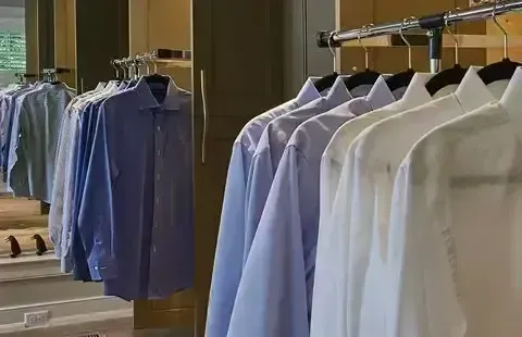 Dress shirts hanging on racks in a clothing store, mostly light blue and white.