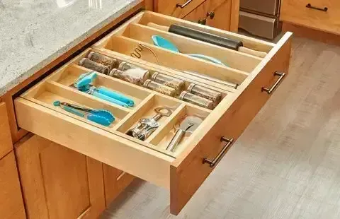 Open kitchen drawer with organized wooden cutlery and utensil trays, including blue-handled tools.