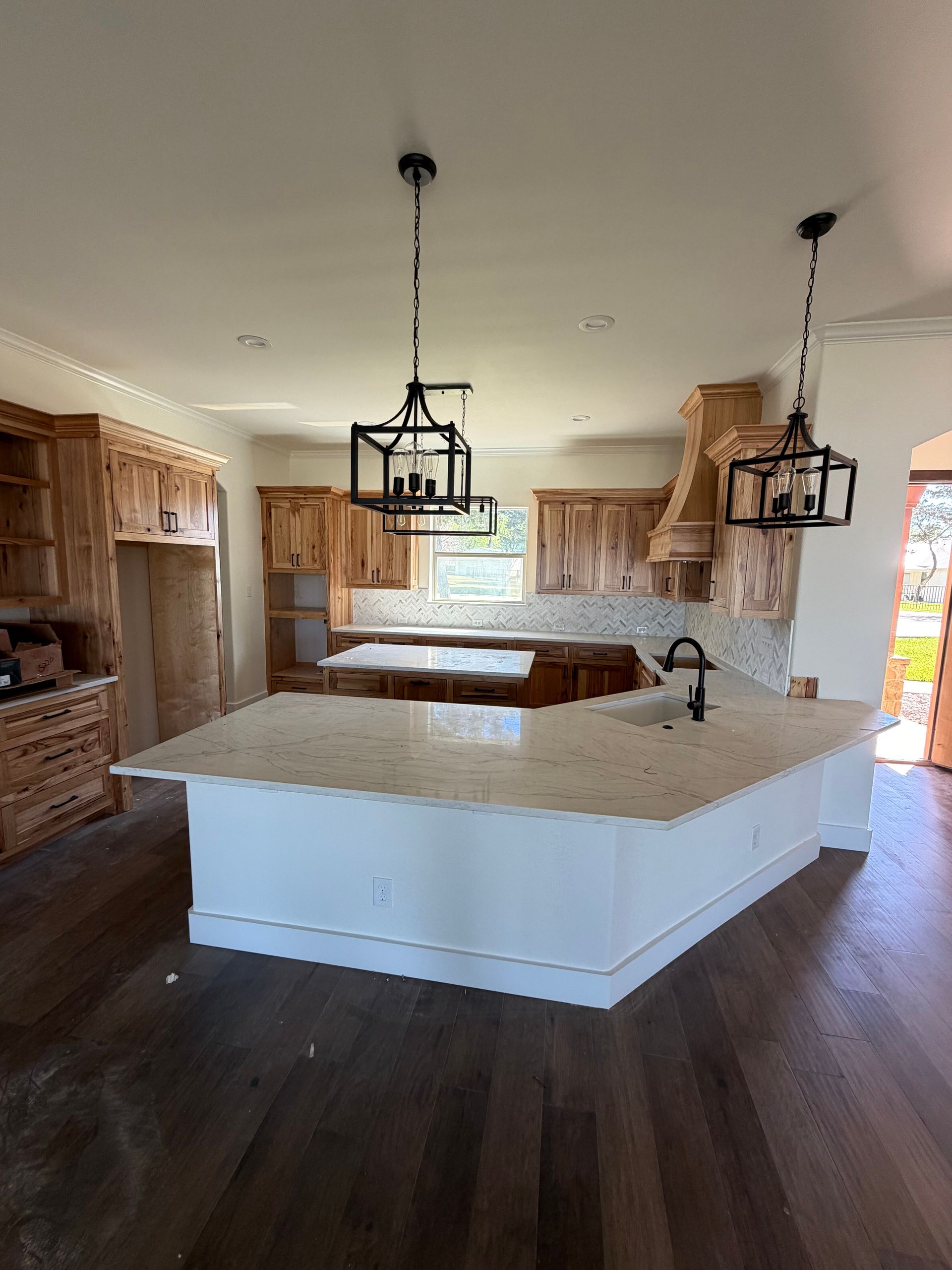 Modern kitchen with large white island, dark wood floors, and hanging lantern pendant lights.