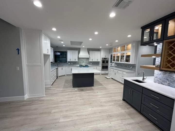 Bright modern kitchen with white cabinets, gray island, and black lower cabinets, viewed from the center.