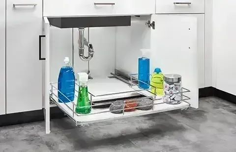Under-counter lab sink with cleaning supplies in blue, green, and yellow bottles on a wire rack