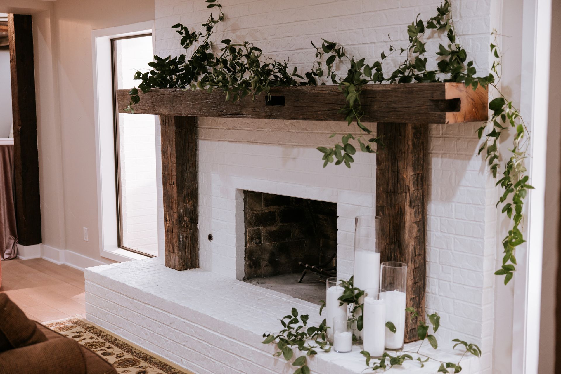 White brick fireplace with wooden mantel, greenery, and candles.