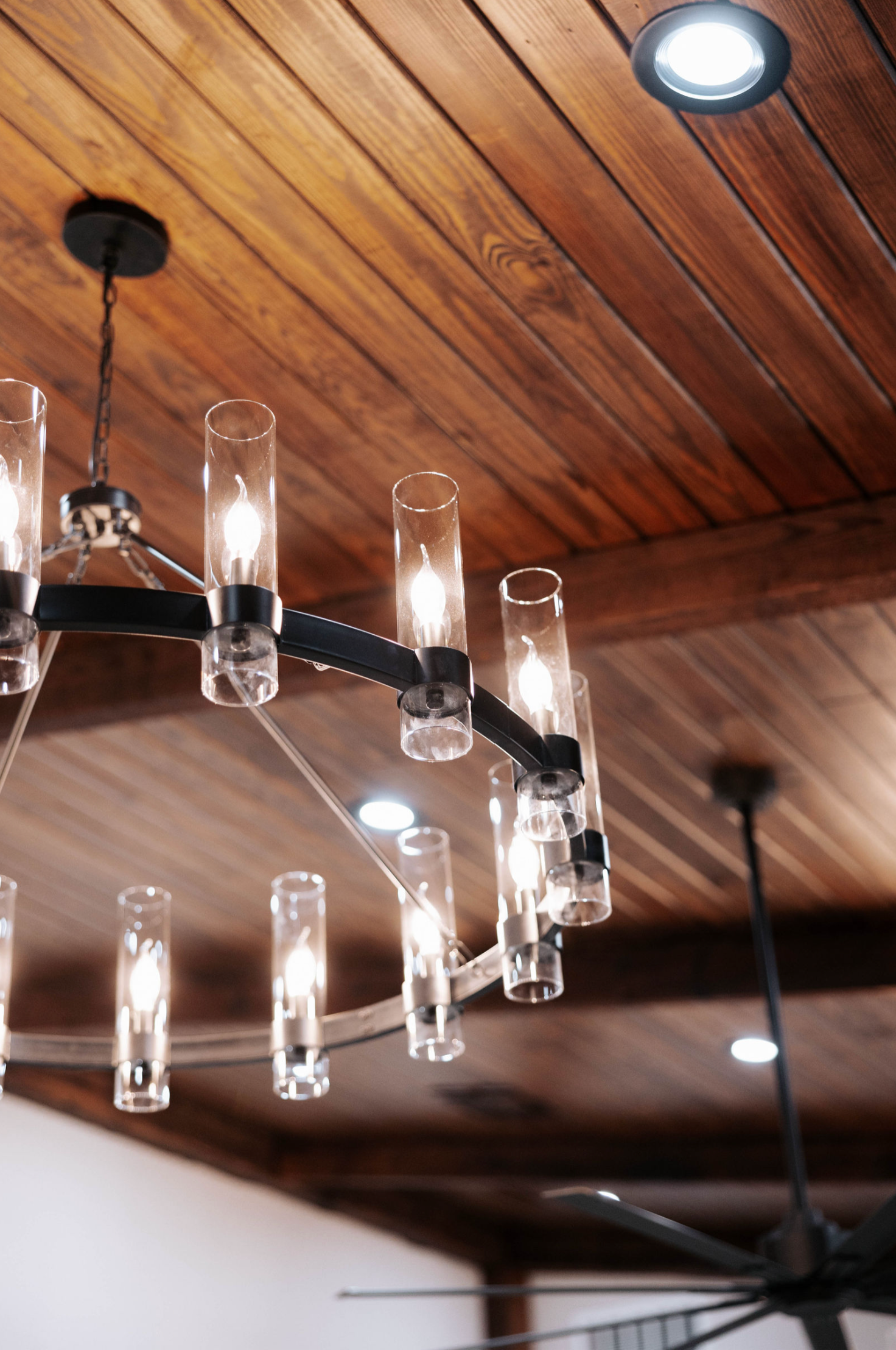 Modern chandelier with cylindrical glass shades, hanging from a wooden, planked ceiling.