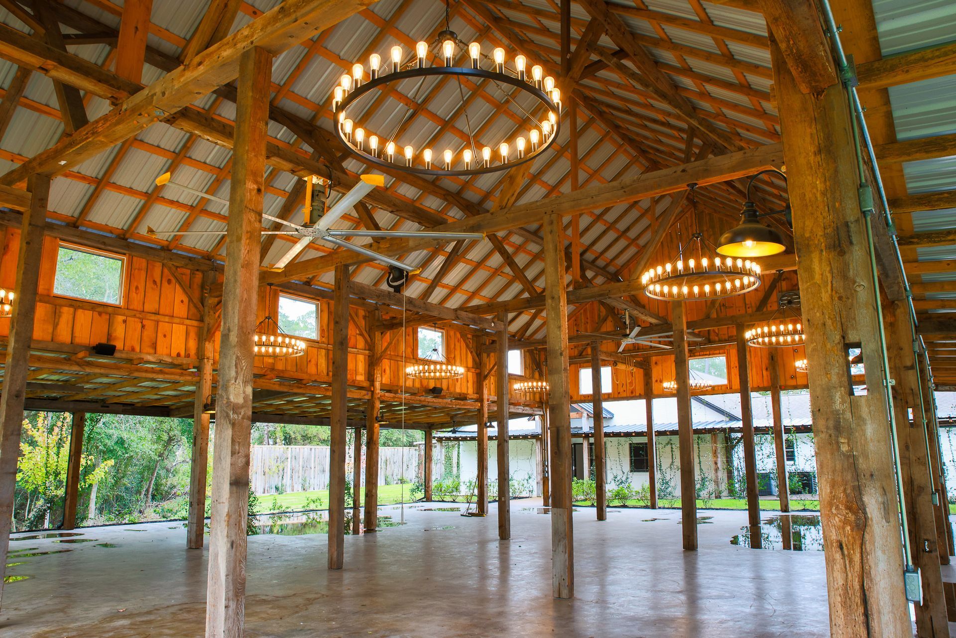 Rustic event space with wooden beams, circular chandeliers, and a concrete floor.