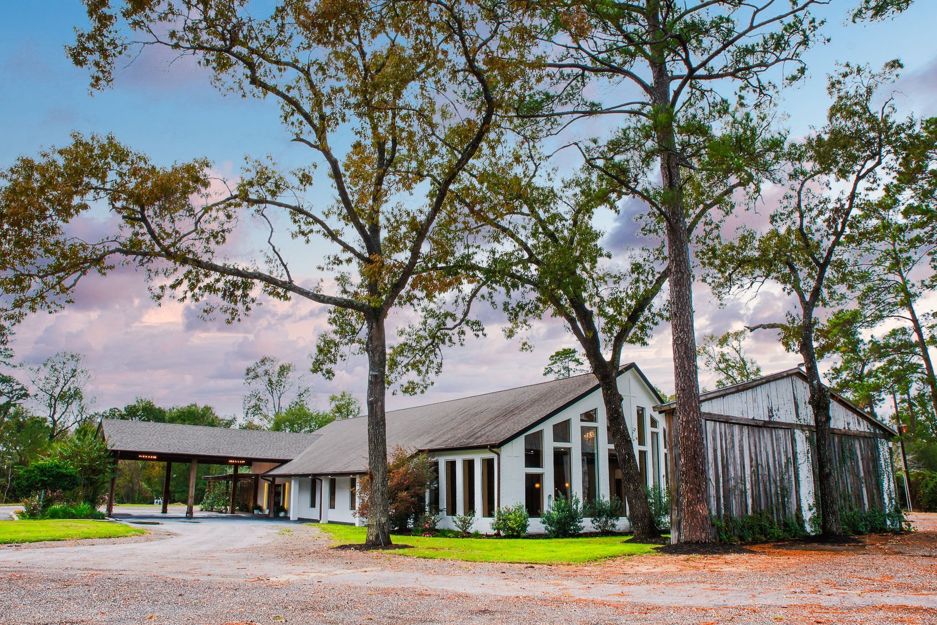 White building with tall windows and a covered entrance, set among trees under a cloudy sky.