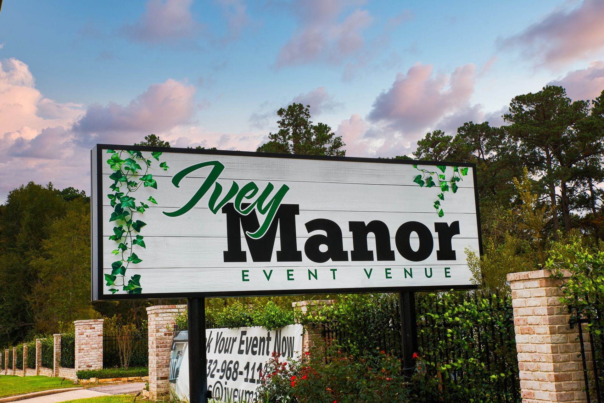 Sign for Ivey Manor Event Venue with green ivy, white background, and brick pillars.