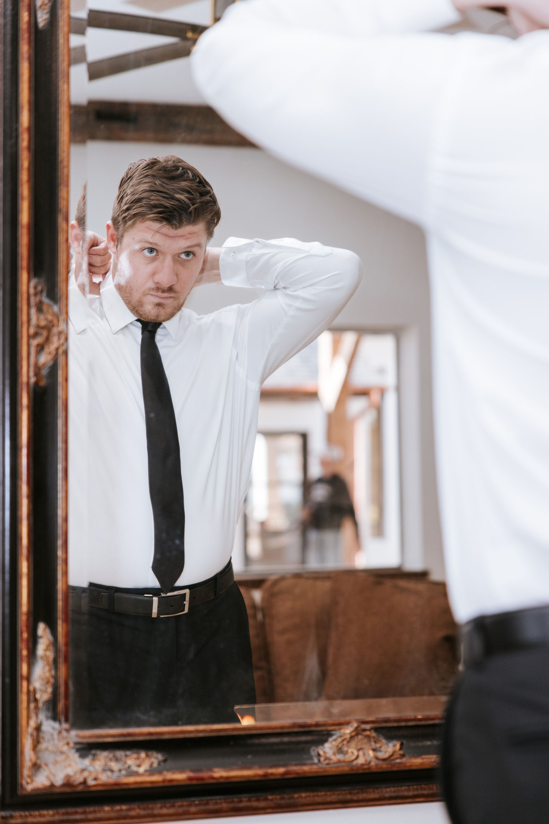 Man in white shirt and black tie adjusting hair in mirror.
