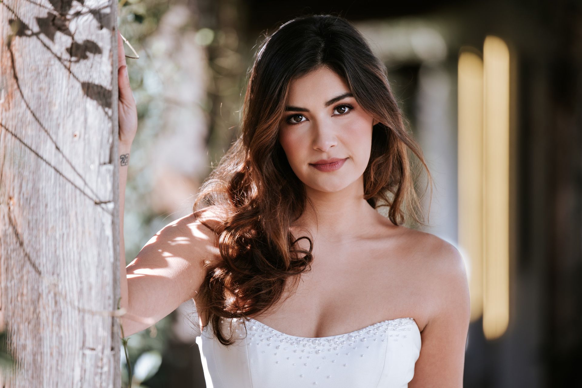 Portrait of a woman in a white strapless dress standing by a stone wall outdoors