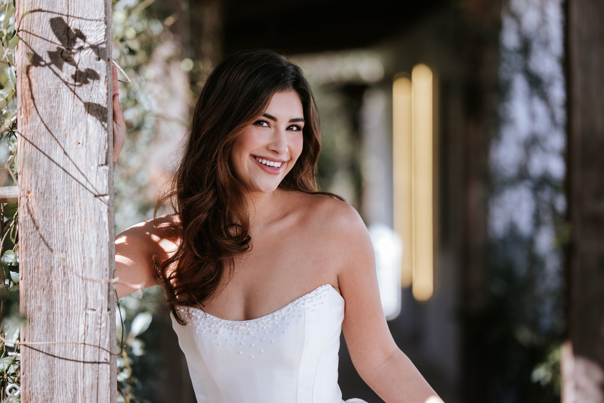 Smiling woman in a white strapless dress standing in a softly lit outdoor corridor
