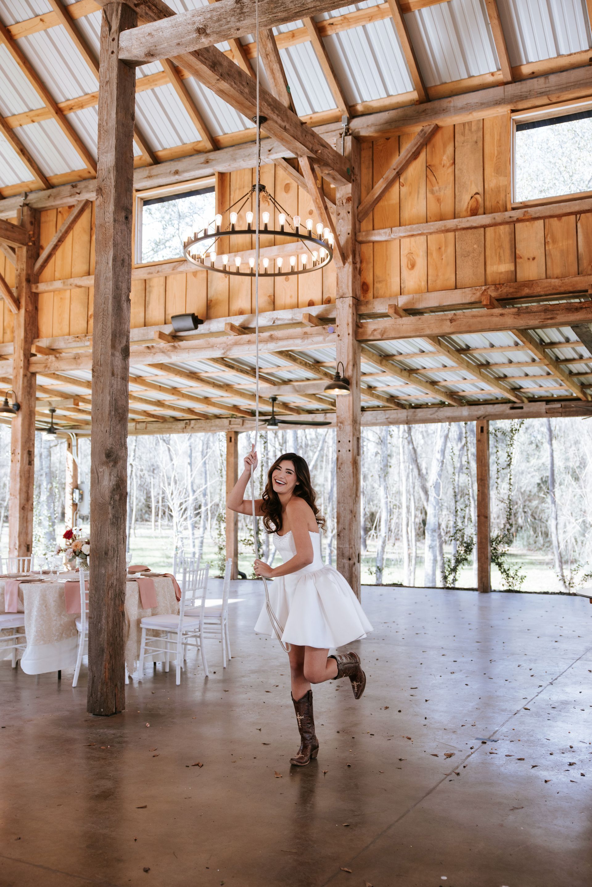 Woman in white dress dancing in a rustic wooden barn with chandeliers and white chairs