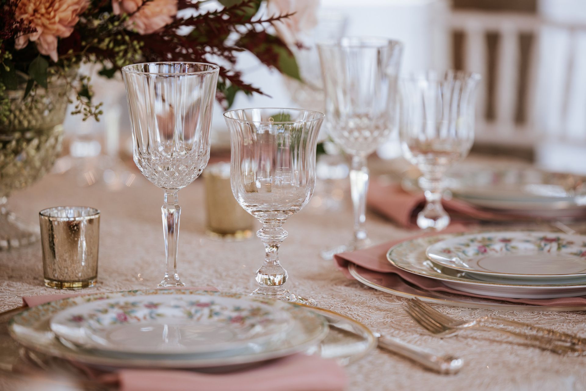 Elegant table setting with pink napkins, crystal glassware, and floral centerpiece on a lace tablecloth