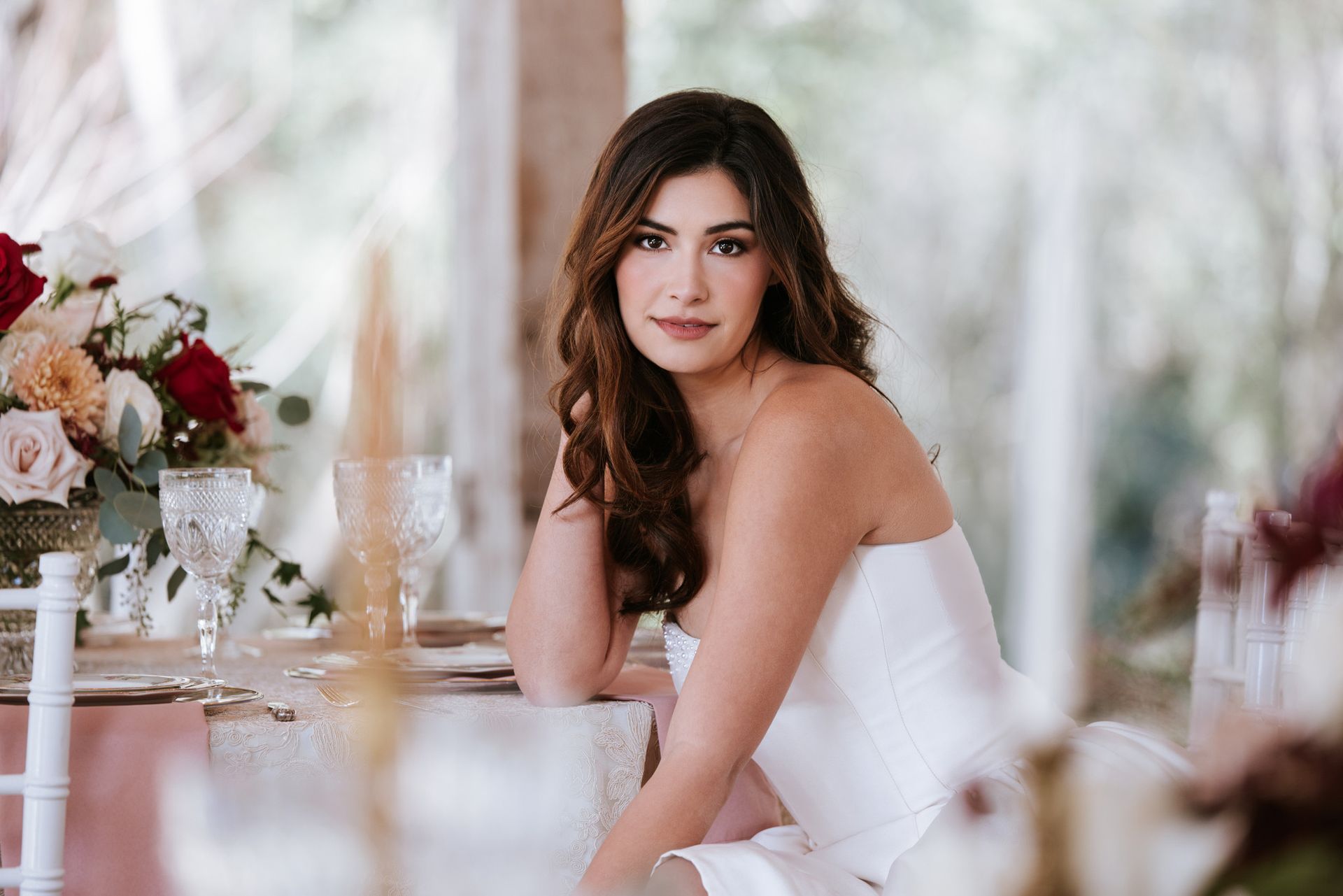 Woman in a white dress seated at a decorated table with flowers in a softly lit room