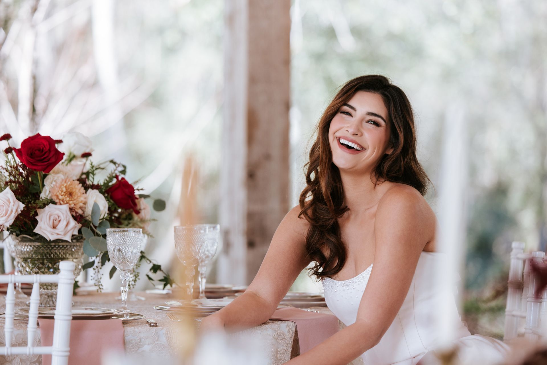 Smiling woman in a white dress seated at a decorated table with flowers in a bright indoor setting