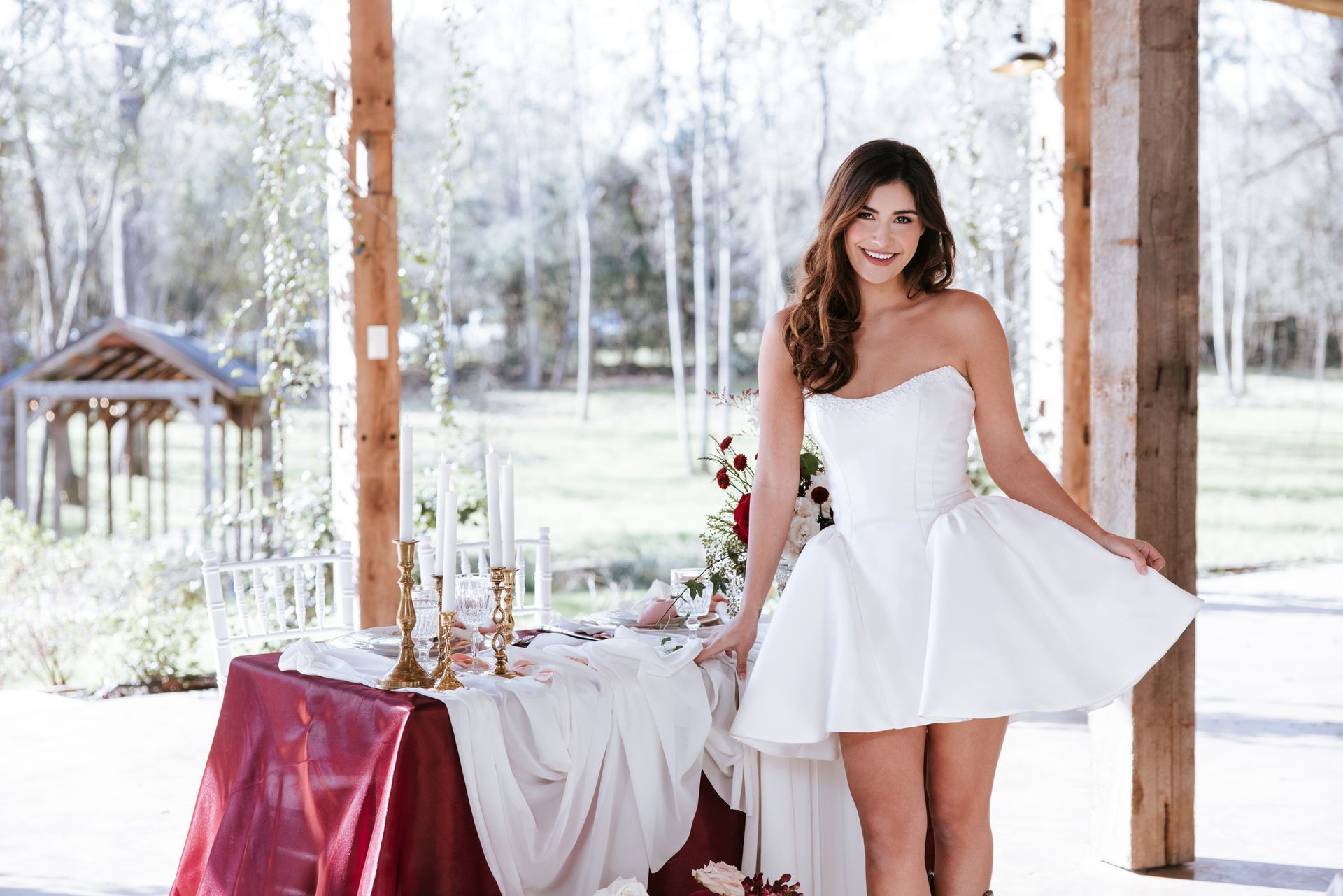 Woman in a white dress standing beside a decorated outdoor table in a bright gazebo