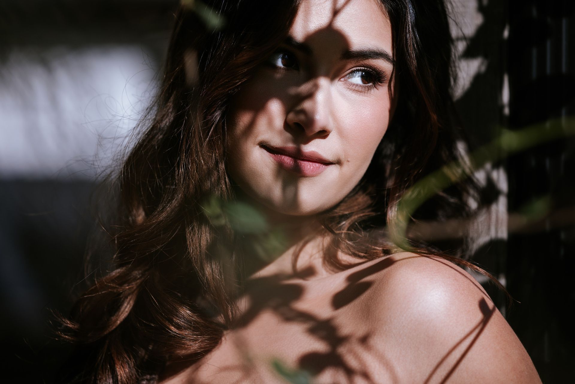 Close-up portrait of a woman with dark hair, lit by soft shadows from leaves